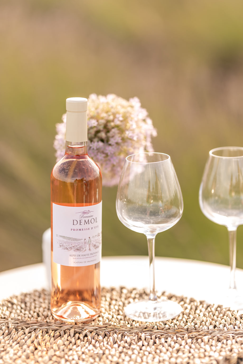 Bouteille de rosé Promesse d'été du Domaine Demol et deux verres sur une table, devant les lavandes