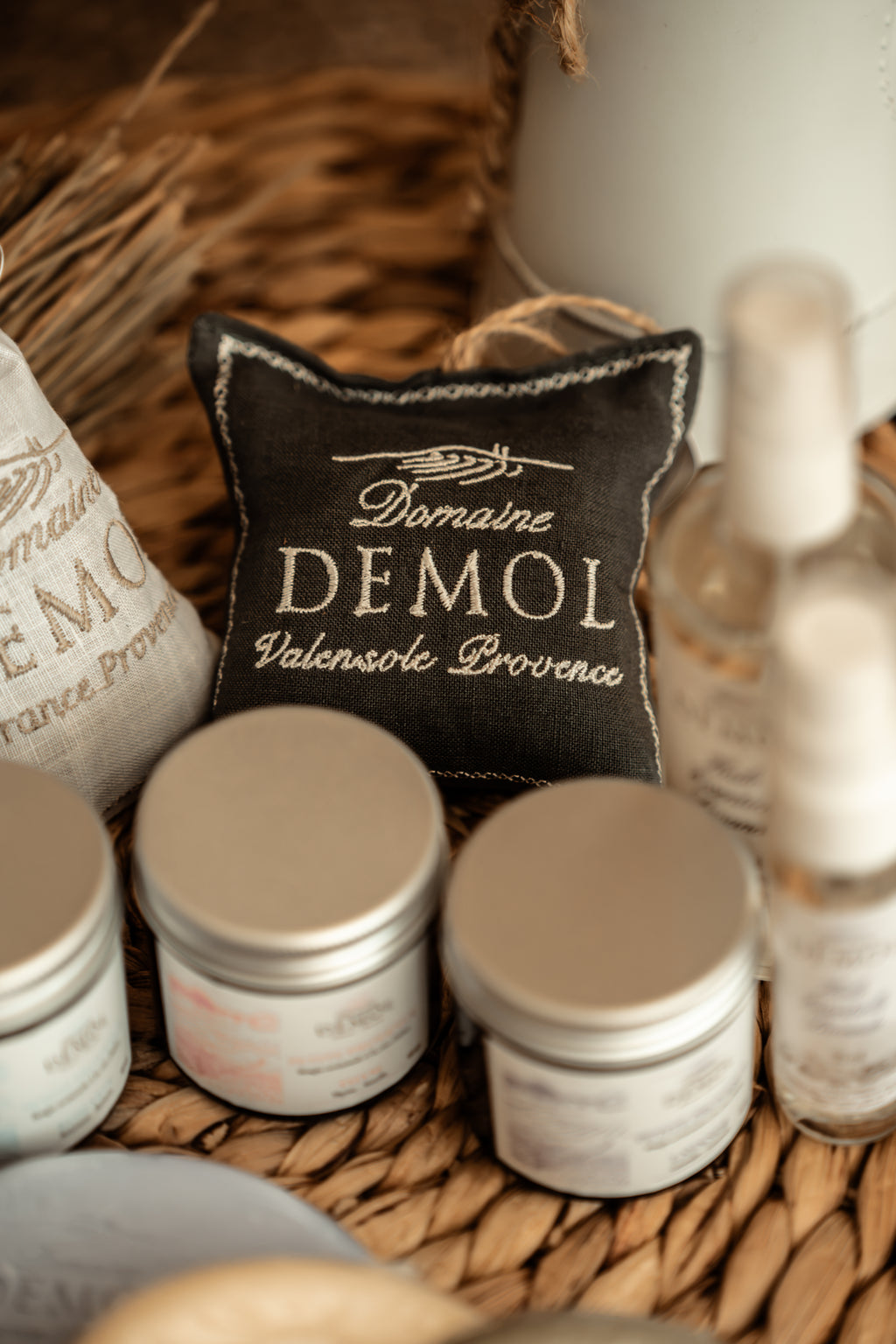 Coussinet de lavande Domaine Demol dans un panier, entouré de bougies en pot et d'un sachet de lavande