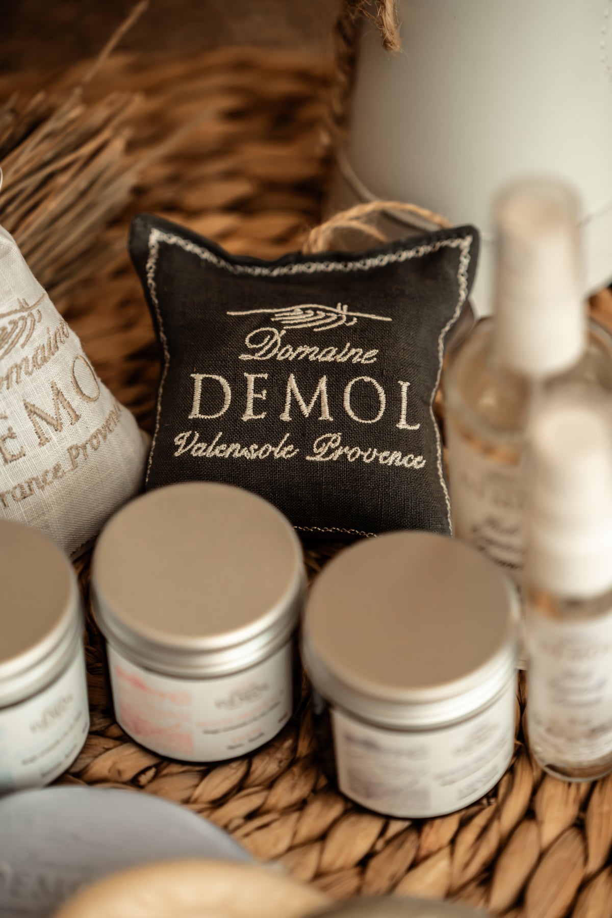 Coussinet de lavande Domaine Demol dans un panier, entouré de bougies en pot et d'un sachet de lavande