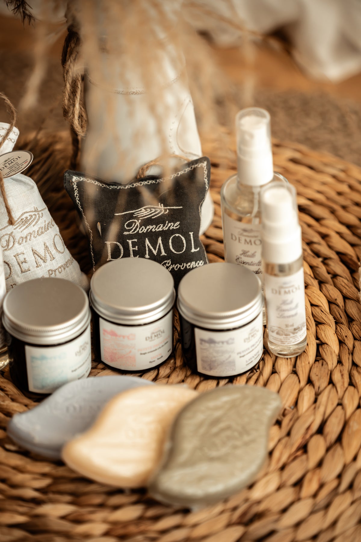 Trois bougies Domaine Demol en pot aluminium, savons et vaporisateurs sur un dessous de plat en fibre