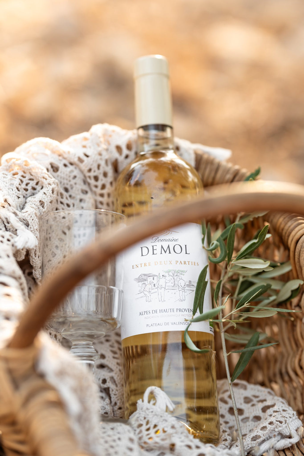 Vin blanc du Domaine Demol présenté dans un panier en osier, avec un rameau d'olivier