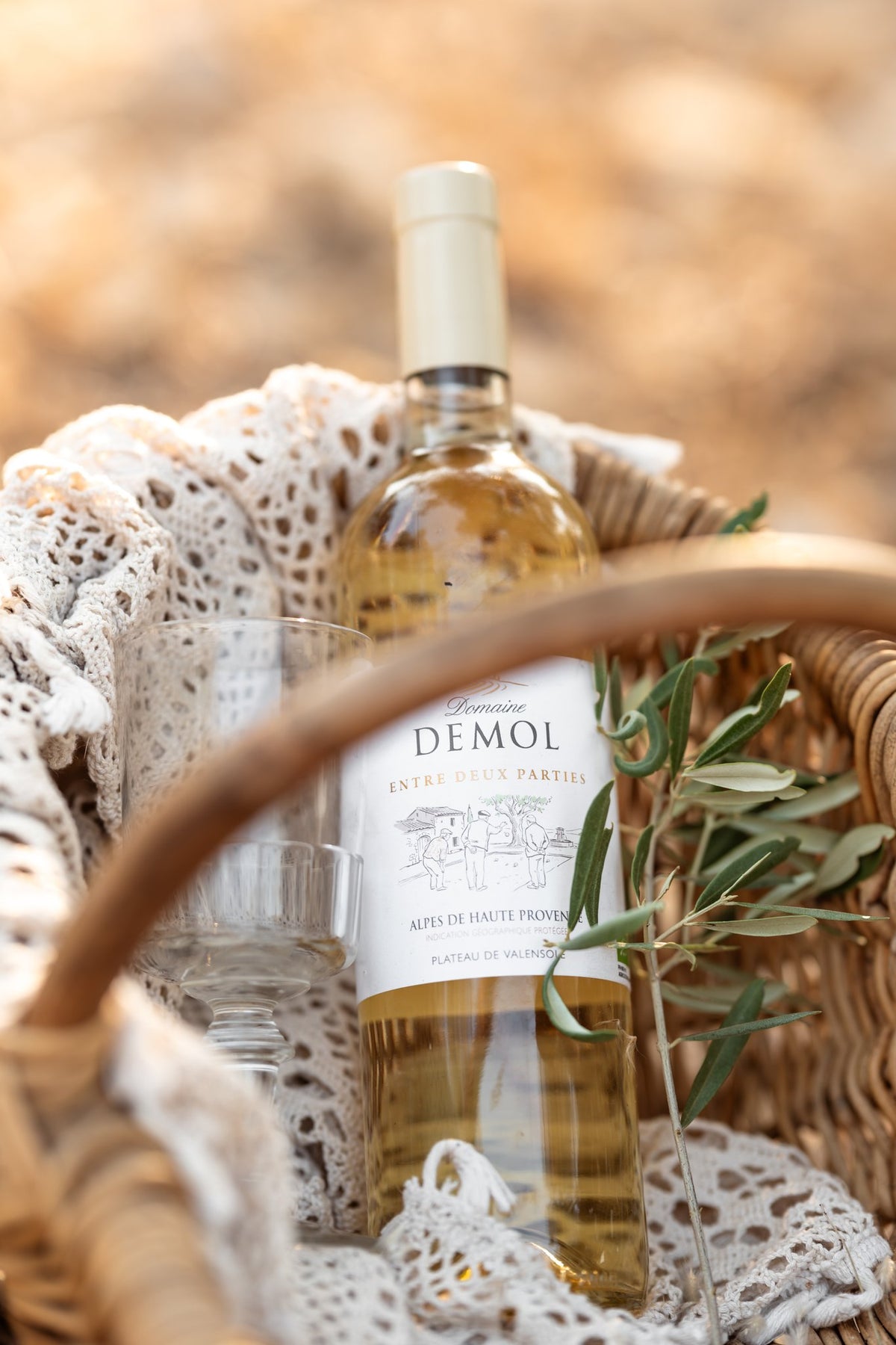 Vin blanc du Domaine Demol présenté dans un panier en osier, avec un rameau d'olivier