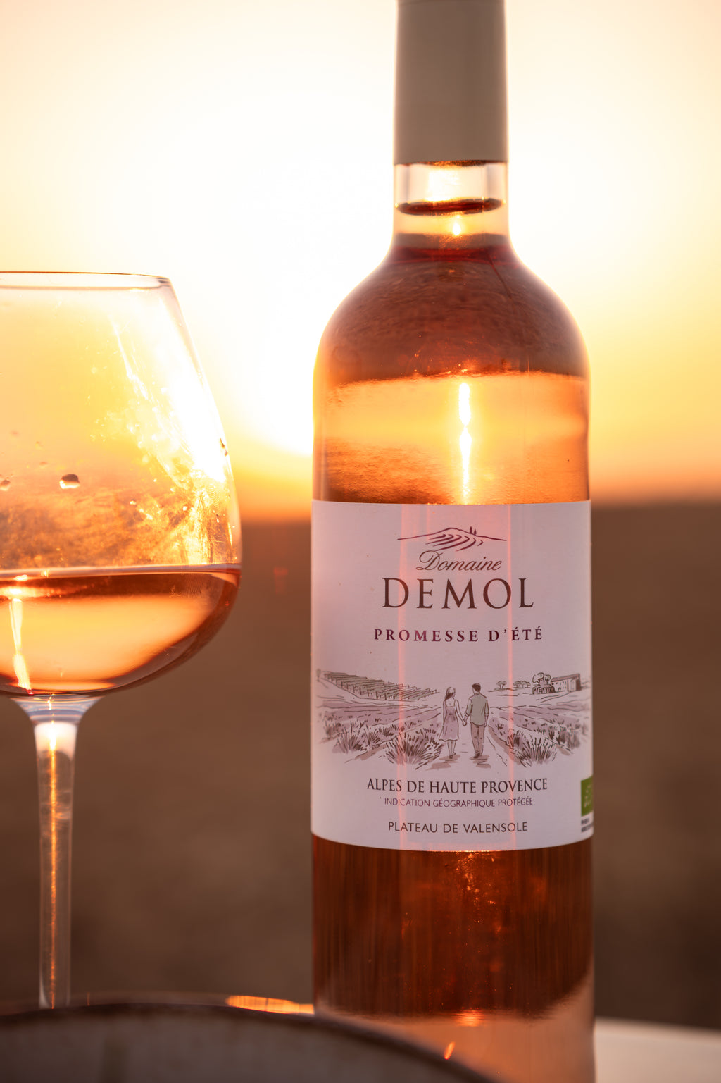 Bouteille de rosé Promesse d'été du Domaine Demol et un verre rempli, au soleil couchant sur le plateau