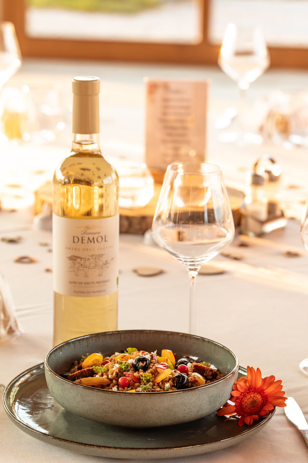 Bouteille de vin blanc du Domaine Demol sur une table dressée, avec un plat de petit épeautre et un verre