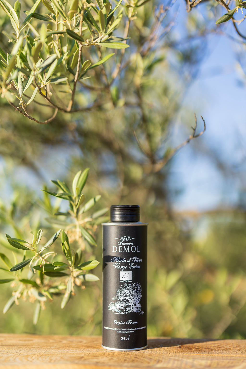 Bouteille de 25 cl d'huile d'olive vierge extra Domaine Demol, étiquette noire, parmi les branches d'olivier