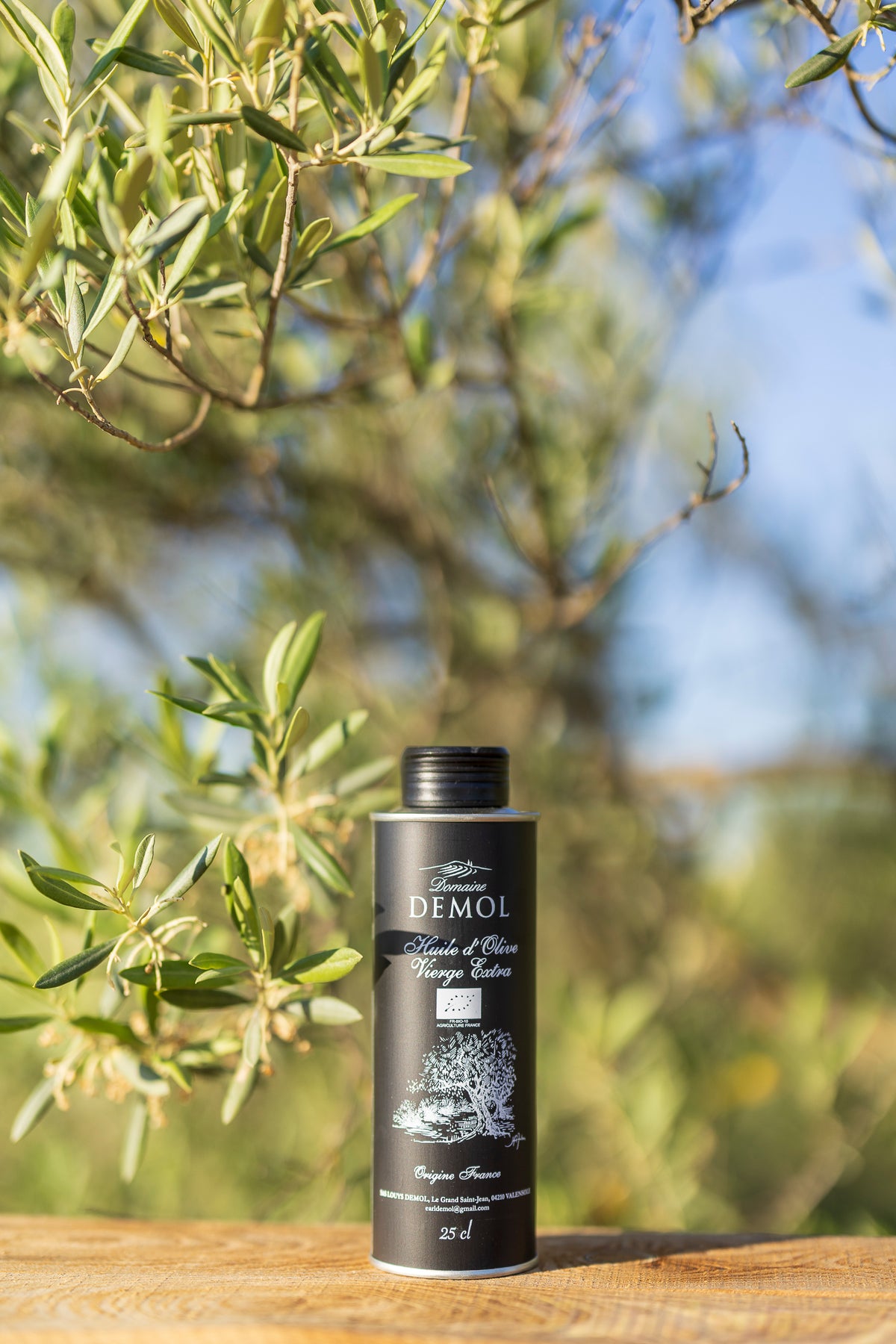 Bouteille de 25 cl d'huile d'olive vierge extra Domaine Demol, étiquette noire, parmi les branches d'olivier