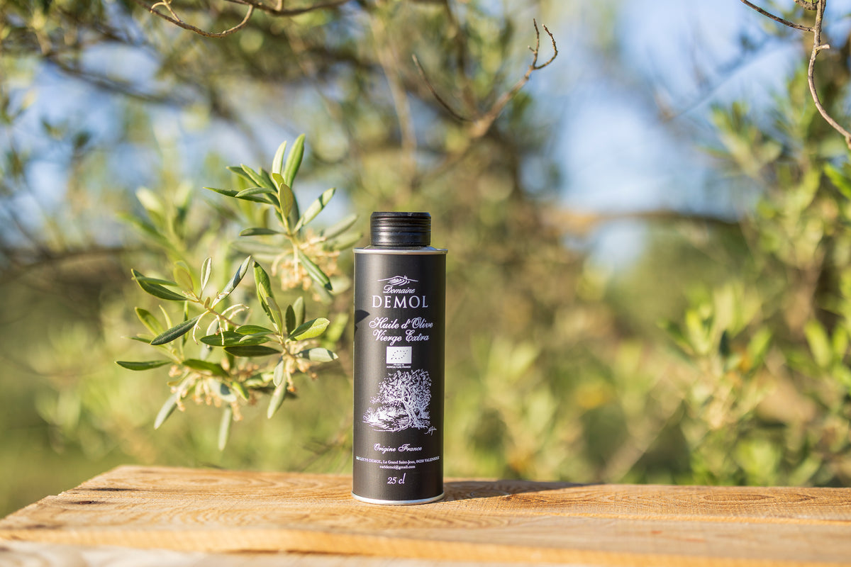 Bouteille de 25 cl d'huile d'olive vierge extra Domaine Demol sur une planche de bois, oliviers en fond