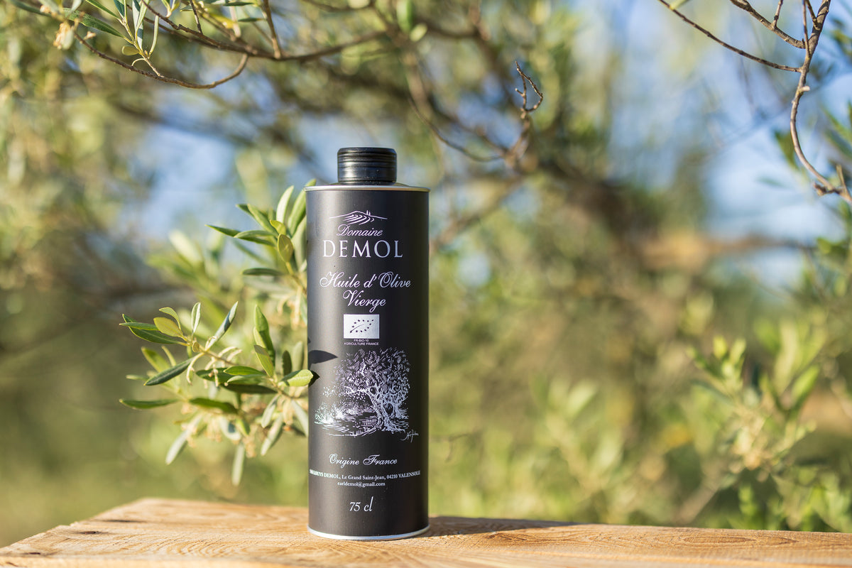 Bouteille de 75 cl d'huile d'olive vierge Domaine Demol posée sur du bois, oliviers en arrière-plan