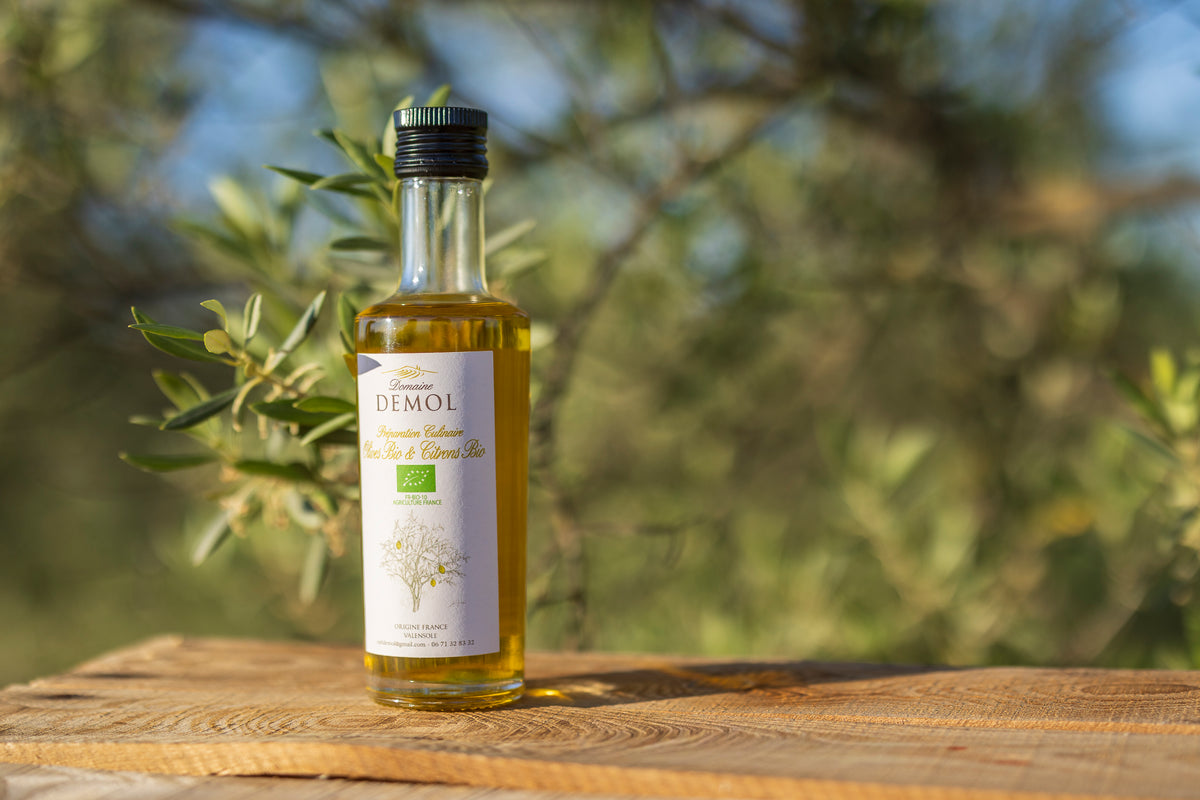 Bouteille d'huile d'olive aux olives et citrons BIO du Domaine Demol posée sur une table en bois