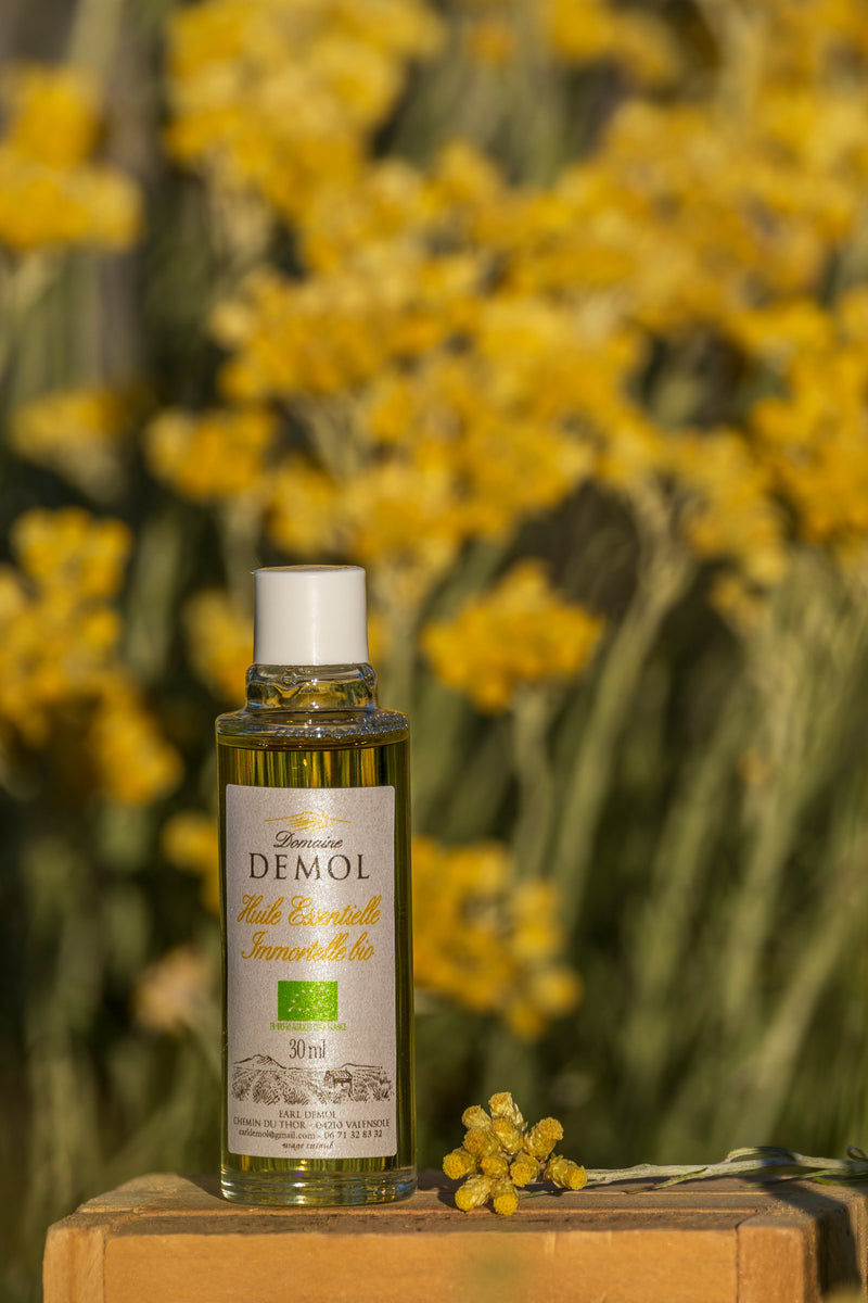Huile essentielle d'immortelle BIO du Domaine Demol devant les fleurs jaunes de l'immortelle
