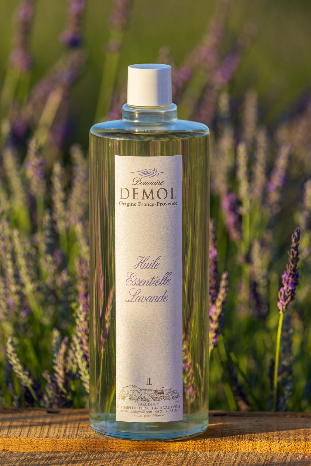 Flacon d'un litre d'huile essentielle de lavande du Domaine Demol, devant les rangs de lavande