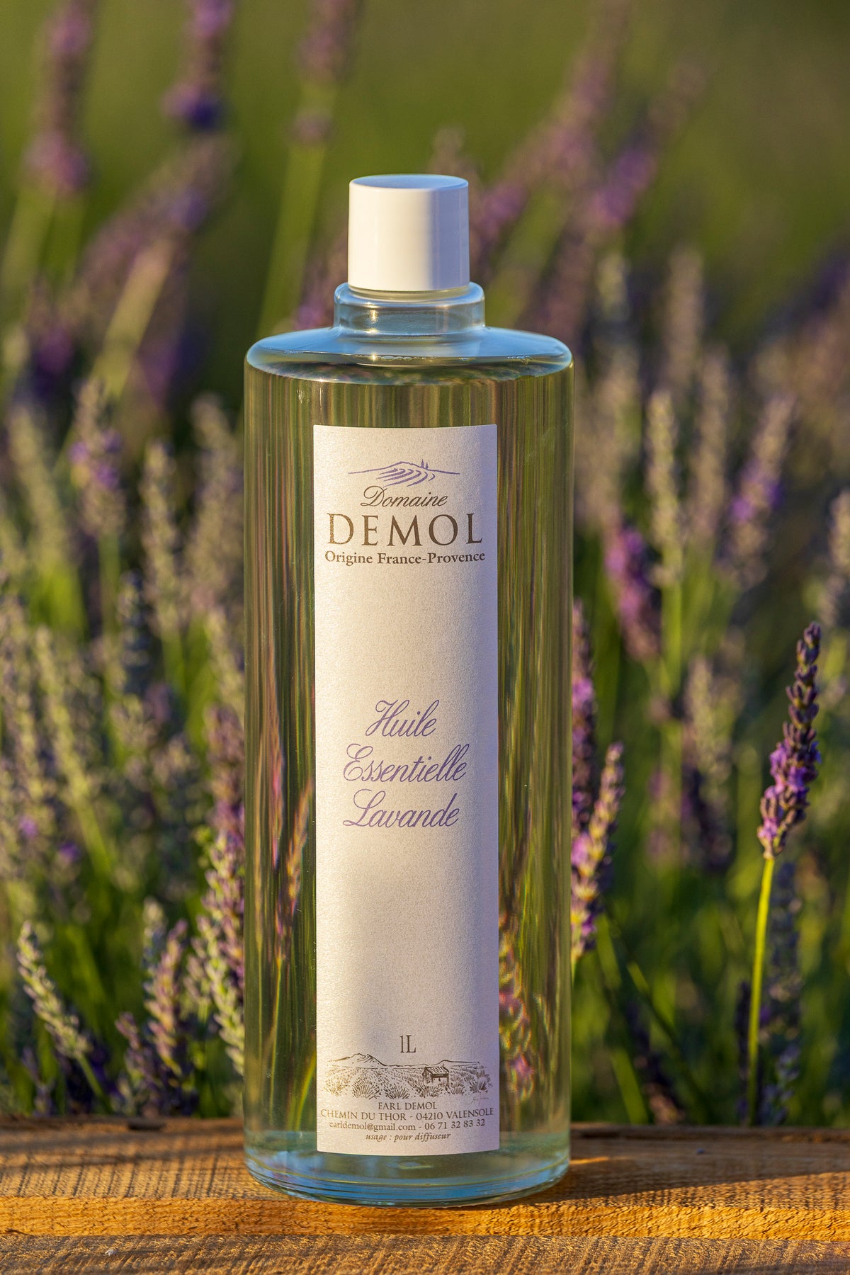 Flacon d'un litre d'huile essentielle de lavande du Domaine Demol, devant les rangs de lavande
