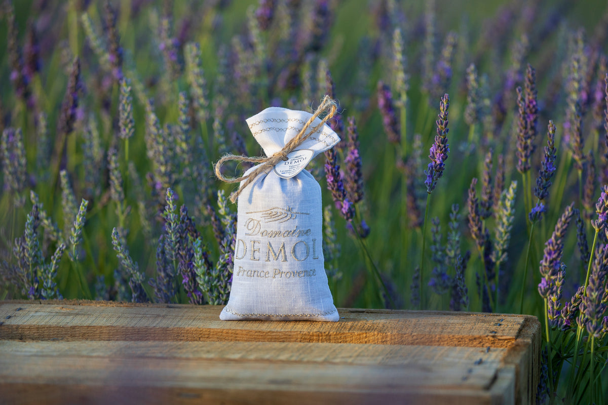Sachet de fleurs de lavande Domaine Demol en lin clair, noué d'une ficelle, devant un champ de lavande
