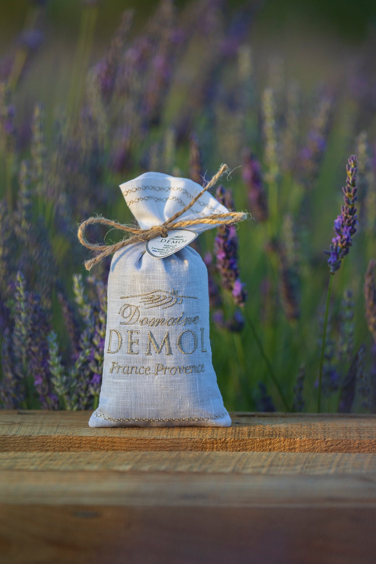 Sachet de fleurs de lavande Domaine Demol en lin brodé, posé sur une poutre en bois dans la lavande
