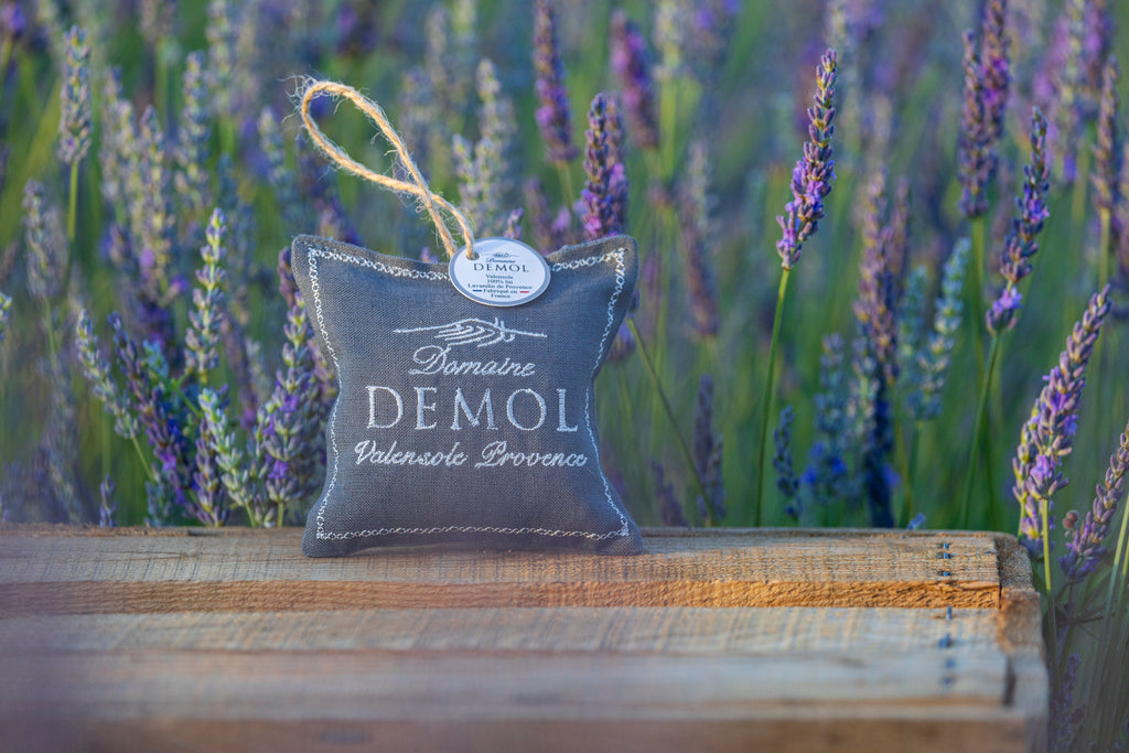 Coussinet de lavande Domaine Demol en toile grise brodée, suspendu à une ficelle, dans un champ de lavande