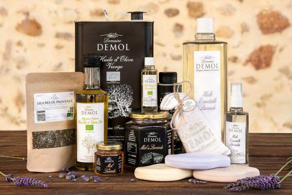 Gamme de produits du domaine Demol posée sur une table en bois : huile d'olive, miel, herbes de Provence, savons